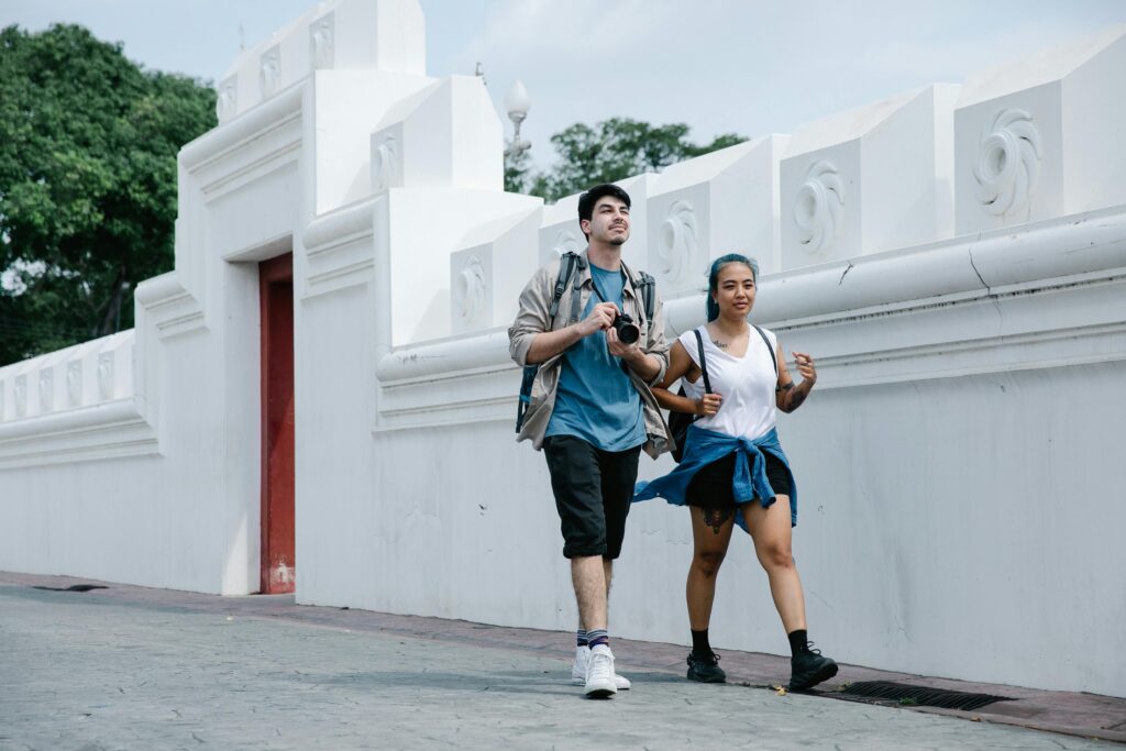 Young tourists exploring a city, walking by a historic white wall on a bright day.
